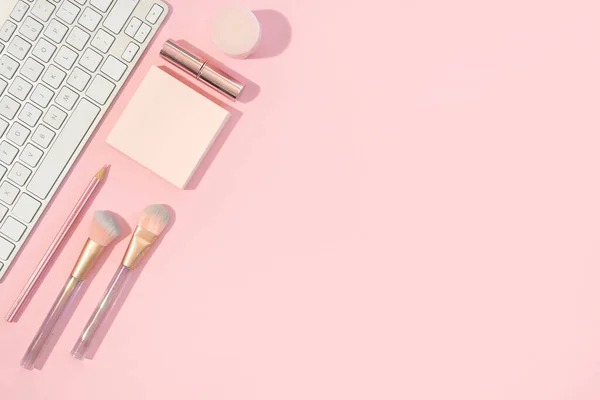 办公室女性办公桌，带有键盘和粉红背景的化妆品配件，平铺有复制空间 图库图片