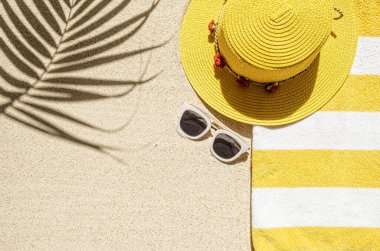 Çizgili sarı ve beyaz havlu çerçeveli kumlu sahil manzarası ve beyaz güneş gözlüğü. Kopyalama alanı ve görünür kum dokusu olan arkaplan.