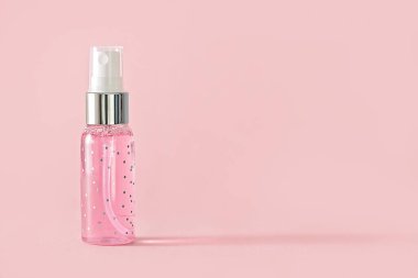Pembe arka planda spreyi olan küçük şeffaf pembe şişe.
