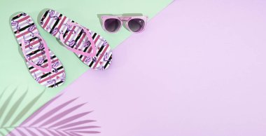 Bir çift yaz sandaleti, parmak arası terlik ve pastel pembe ve yeşil arka planda pembe güneş gözlüğü. Palmiye yaprağı gölgesi, üst manzara, kopyalama alanı.