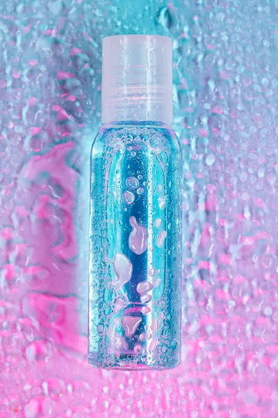 水滴在粉色和蓝色背景上的透明小瓶子，顶部视图，垂直构图 — 图库照片