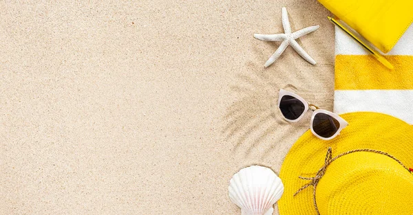 Top view of sandy beach with stripy yellow and white towel frame, white sunglasses and sea shells. Background with copy space and visible sand texture. Summer concept Stock Picture