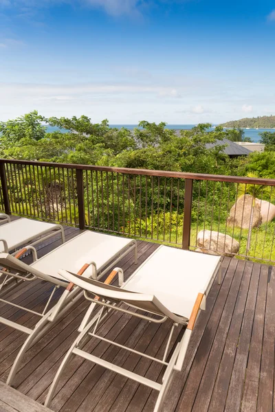 Sillas para tomar el sol en la cubierta de madera con vista al mar azul — Foto de Stock