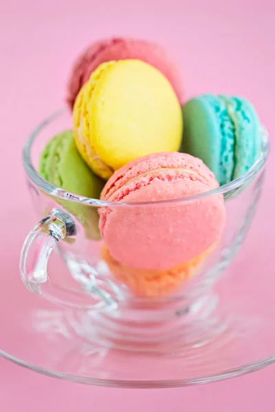 Colorful French macaroons in glass cup on pink background — Stock Photo, Image