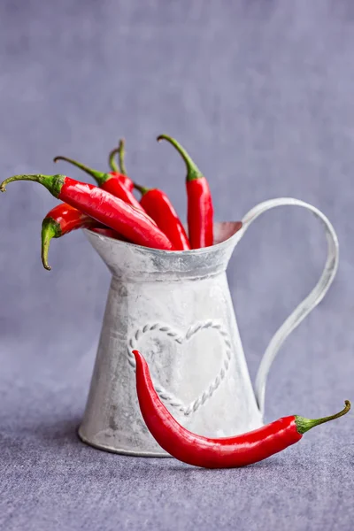 Chiles rojos picantes en una canasta gris metálica sobre fondo azulado — Foto de Stock