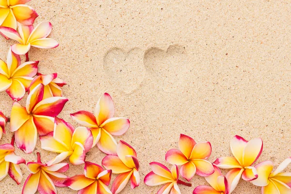 Två hjärta skriva ut på sand med frangipani blommor, ovanifrån, vågrät — Stockfoto