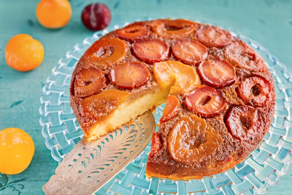 Homemade upside-down plum cake on glass plate and blue backgroun — Stock Photo, Image