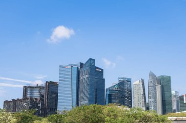 Singapur 'daki modern gökdelenlerin yer aldığı göz kamaştırıcı bir gökyüzü manzarası, yemyeşil ve açık mavi gökyüzü ile çevrili, kentsel mimari ve doğa sergileniyor.