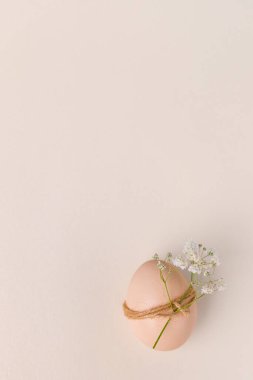 Bir yumurta sicimle sarılır ve küçük beyaz çiçeklerle süslenir, yumuşak bir pastel arka plana yerleştirilir, minimalist estetik bir paskalya bavulu yaratır.