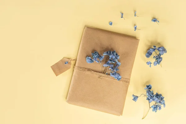 Hüner kağıdına sarılı bir hediye. Kırbaçla bağlanmış ve kurutulmuş menekşe rengi ortanca çiçekleri hediye kutusuyla süslenmiş. Ya da Anneler Günü ya da Sevgililer Günü için sarı arka planda bir hediye. İlkbahar. 8 Mart.