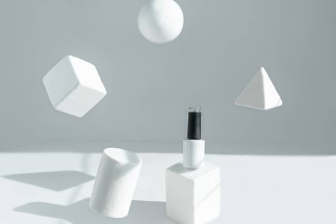 Havalanma. Beyaz bir şişe beyaz bir kaidede duruyor, geometrik şekiller havada asılı duruyor..