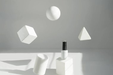 Havalanma. Beyaz bir şişe beyaz bir kaidede duruyor, geometrik şekiller havada asılı duruyor..