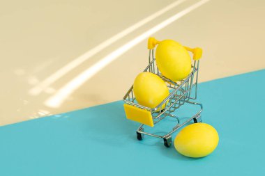 Sarı-mavi arka planda süpermarket tramvayındaki sarı paskalya yumurtaları. Tatil alışverişi konsepti