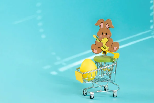 Süpermarketin tramvayında sarı bir yumurta ve tahta bir oyuncak var. Fırçalı bir Paskalya tavşanı ve pençelerinde bir yumurta.