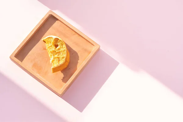 Açık kahverengi tabakta pembe arka planda kurumuş portakallar. Bir tabakta portakal dilimlerinin yakın çekimi