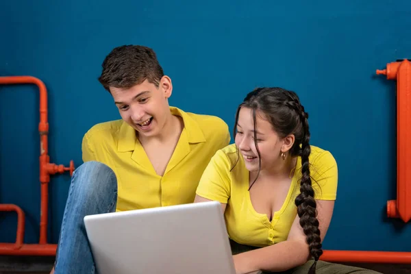 Gençler bilgisayarda bir başvuru aracılığıyla oturup konuşuyorlar. Bir erkek ve bir kız ellerinde dizüstü bilgisayarla yerde oturmuş video izliyorlar ya da ortak bir proje hazırlıyorlar..