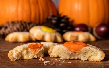Arka planda portakal kabakları ve çam kozalakları olan ahşap masada sonbahar kurabiyeleri.