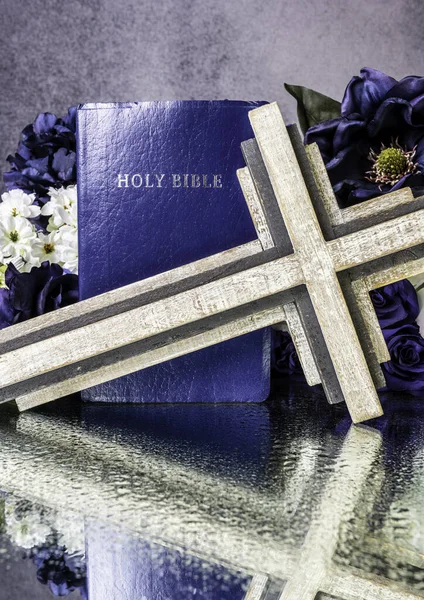 blue bible surrounded by stones and flowers reflecting on wet mirror