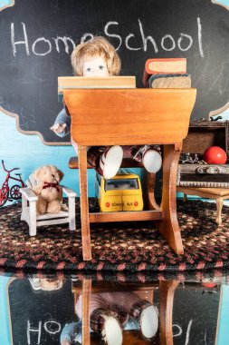 Küçük masadaki oyuncak bebek hayatı ve oyuncaklarla çevrili evde okutulan bir yığın kitap.