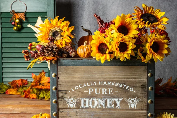 wooden box full of fall decorations including yellow sunflowers orange pumpkins and autumn leaves