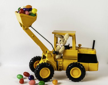 Paskalya tavşanı, beyaz arka planda içi jelibon dolu sarı oyuncak yükleyici kullanıyor.