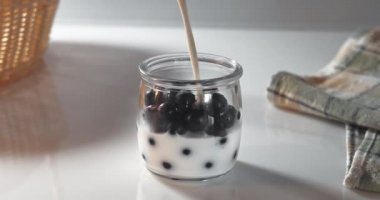 Süt taze böğürtlenlerle dolu bir kavanoza dökülür. Sabah kahvaltısı için ev yapımı yoğurt hazırlıyorum.