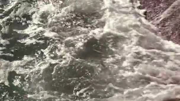 Mořské vlny s bílou pěnou se valí na písčitém břehu, odraz slunce ve vodě. Černé moře