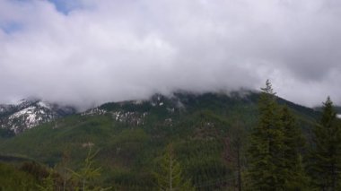 Karda dağlar, odunla kaplanmış. Dağların üzerinde kalın bulutlar. Montana, ABD