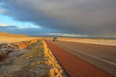 NEW MEXICO, ABD - 22 Kasım 2019: New Mexico 'daki Guadalupe Dağları' nın arka planında, kırmızı günbatımında ve gök gürültülü bulutlarda yol alan araba