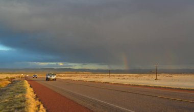 NEW MEXICO, ABD - 22 Kasım 2019: New Mexico 'daki Guadalupe Dağları' nın arka planında, kırmızı günbatımında ve gök gürültülü bulutlarda yol alan araba