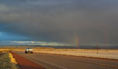NEW MEXICO, ABD - 22 Kasım 2019: New Mexico 'daki Guadalupe Dağları' nın arka planında kırmızı gün batımında gökkuşağı ve araba