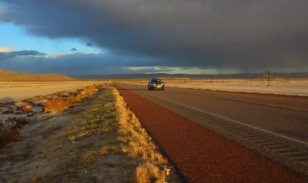 NEW MEXICO, ABD - 22 Kasım 2019: New Mexico 'daki Guadalupe Dağları' nın arka planında, kırmızı günbatımında ve gök gürültülü bulutlarda yol alan araba