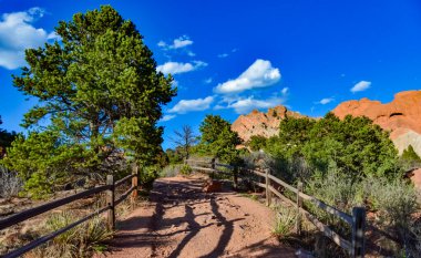Üzerinde güneşin gölgesi olan ahşap bir çit. Kırmızı dağ oluşumlarının arka planında bir insan yürüyor. Colorado Springs Bölgesi Tanrıların Bahçesi, Ulusal Doğal Kent Simgesi 