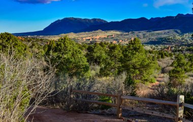 Üzerinde güneşin gölgesi olan ahşap bir çit. Kırmızı dağ oluşumlarının arka planında bir insan yürüyor. Colorado Springs Bölgesi Tanrıların Bahçesi, Ulusal Doğal Kent Simgesi 