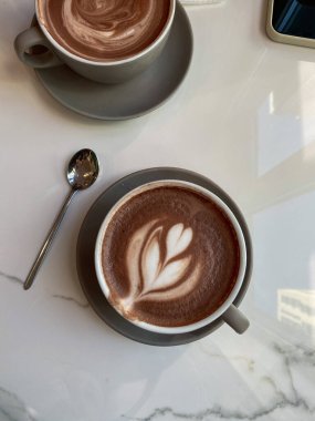 Bir fincan sıcak kahve. Mükemmel bir sabah. Lezzetli latte. Bir kahve dükkanında. Kaşık ve kupa masanın üstünde..