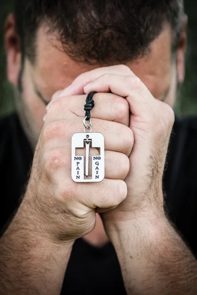 Hombre rezando afuera sosteniendo una pulsera de cruz Imagen de archivo