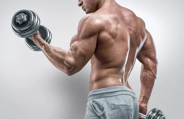 Power athletic man in training pumping up muscles with dumbbells — Stock Photo, Image