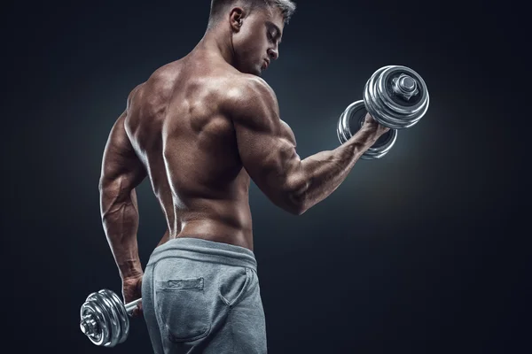 Power athletic man in training pumping up muscles with dumbbells — Stock Photo, Image