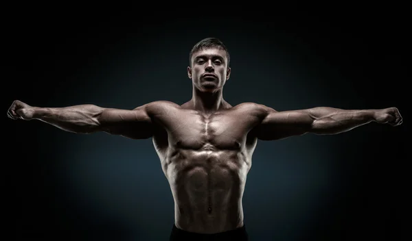 Bonito fisiculturista muscular posando e mantendo os braços estendidos — Fotografia de Stock