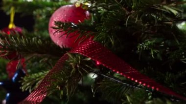 Dallardaki Noel Oyuncakları. Parlak parlak çelenklerle süslenmiş Noel ağacı dalları ve Noel süslemeleri kameranın önünde yavaşça hareket ediyor