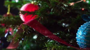 Parlak Noel Oyuncakları. Parlak parlak çelenklerle süslenmiş Noel ağacı dalları ve Noel süslemeleri kameranın önünde yavaşça hareket ediyor
