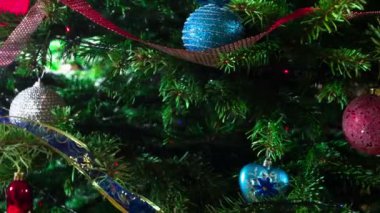 Noel ağacında çelenkler ve oyuncaklar. Parlak parlak çelenklerle süslenmiş Noel ağacı dalları ve Noel süslemeleri kameranın önünde yavaşça hareket ediyor