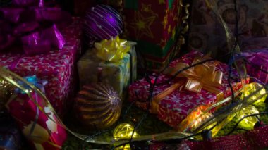 Şirin Noel gelenekleri. Kamera, parıltılı fiyonklarla süslenmiş hediye kutuları, Noel ağacı süslemeleri ve ışıltılı çelenklerle yavaşça hareket ediyor.