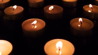 Bir sürü Küçük Mum. Kamera, zifiri karanlıkta yanan küçük mumlarla sahada yavaşça hareket ediyor. Havanın hareketi ile hareket eden alevler. 120fps hızla çekilmiştir.