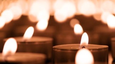 Romantik Mum Ateşi. Kamera, yanan mum grubunun yanından yavaşça geçiyor. Mum ışıkları havanın hareketinden titriyor.