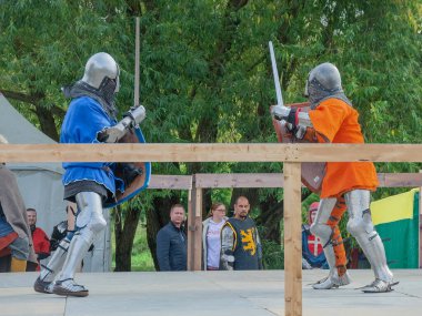 Tver / Rusya - 29 Eylül 2020: Ağır zırhlı savaşçılar kılıçlarla savaşıyor. Arka planda, hakem ve seyirciler. Ortaçağ Avrupa şövalye turnuvalarının tarihi yeniden yapılandırması