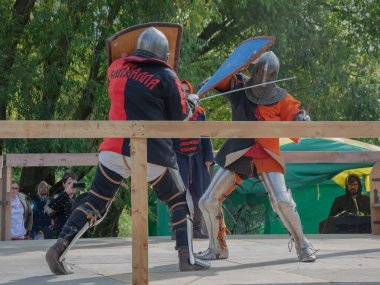 Tver / Rusya - 29 Eylül 2020: Ağır zırhlı savaşçılar kılıçlarla savaşıyor. Arka planda, hakem ve seyirciler. Ortaçağ Avrupa şövalye turnuvalarının tarihi yeniden yapılandırması