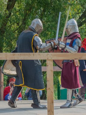 Tver / Rusya - 29 Eylül 2020: Ağır zırhlı savaşçılar kılıçlarla savaşıyor. Arka planda, hakem ve seyirciler. Ortaçağ Avrupa şövalye turnuvalarının tarihi yeniden yapılandırması