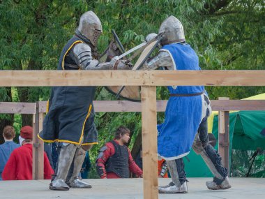 Tver / Rusya - 29 Eylül 2020: Ağır zırhlı savaşçılar kılıçlarla savaşıyor. Arka planda, hakem ve seyirciler. Ortaçağ Avrupa şövalye turnuvalarının tarihi yeniden yapılandırması