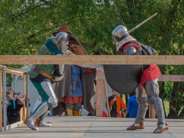 Tver / Rusya - 29 Eylül 2020: Ağır zırhlı savaşçılar kılıçlarla savaşıyor. Arka planda, hakem ve seyirciler. Ortaçağ Avrupa şövalye turnuvalarının tarihi yeniden yapılandırması